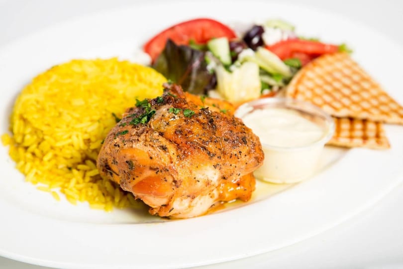 Grilled chicken with yellow rice, a side salad, pita bread, and a dipping sauce.