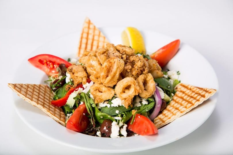 Crispy fried calamari and shrimp on a fresh green salad with tomatoes, feta, olives, and pita.